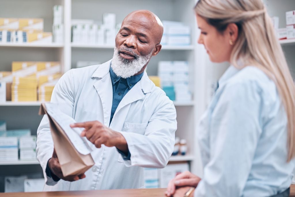 A modern, well-designed on-site clinic pharmacy with a pharmacist actively helping a patient at the counter.